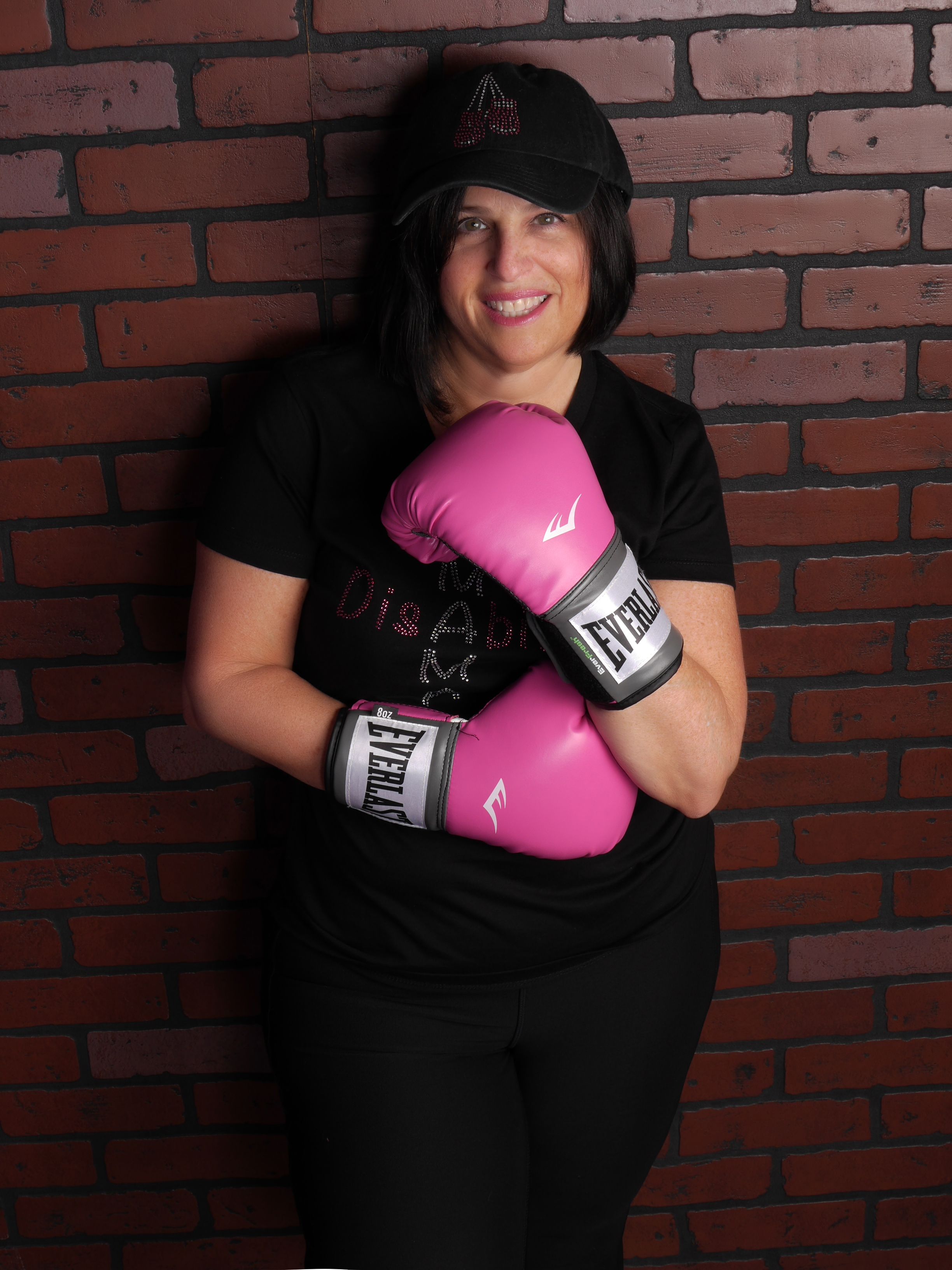 Nadine Vogel against brick wall wearing all black clothing and cap, and pink boxing gloves